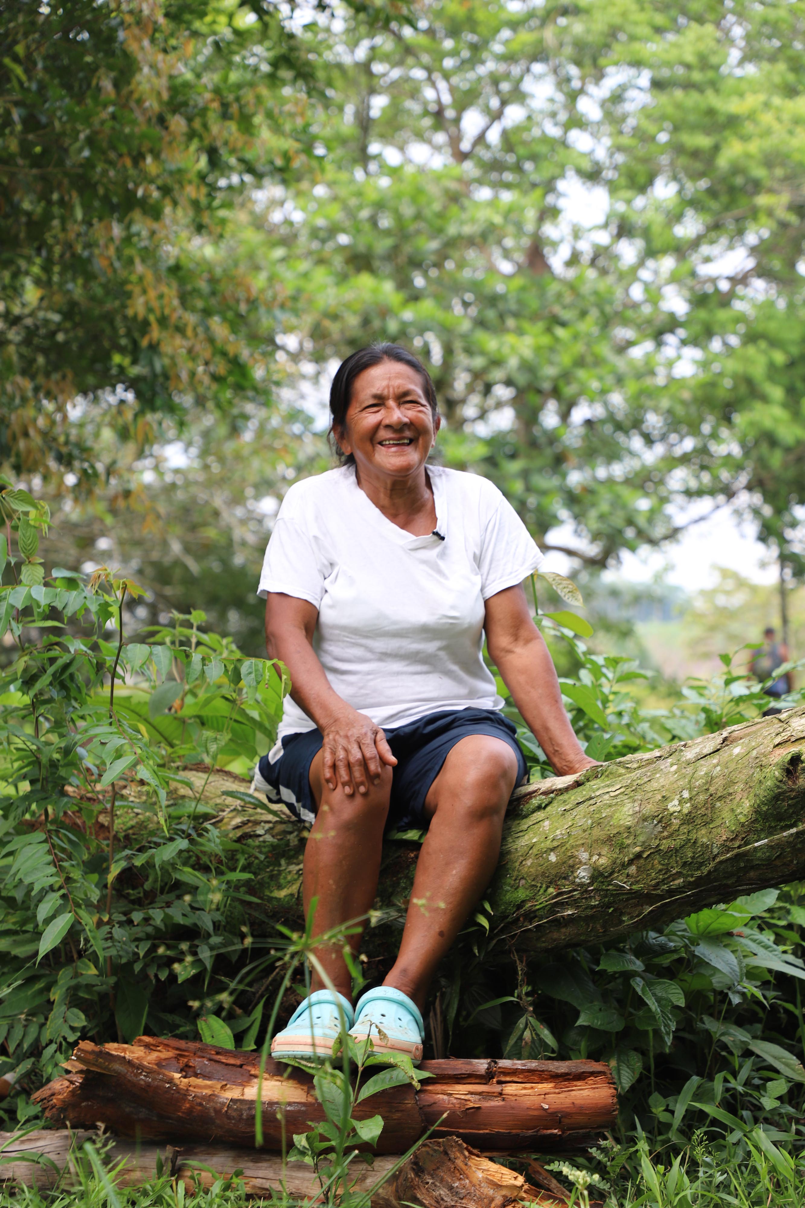 A woman sits on a felled tree smiling.