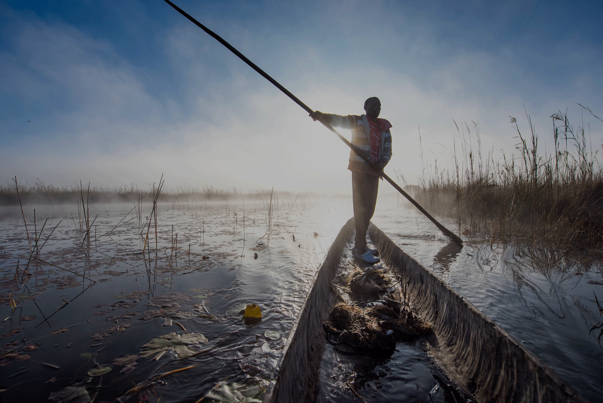 A person canoeing standing up with a long pole.