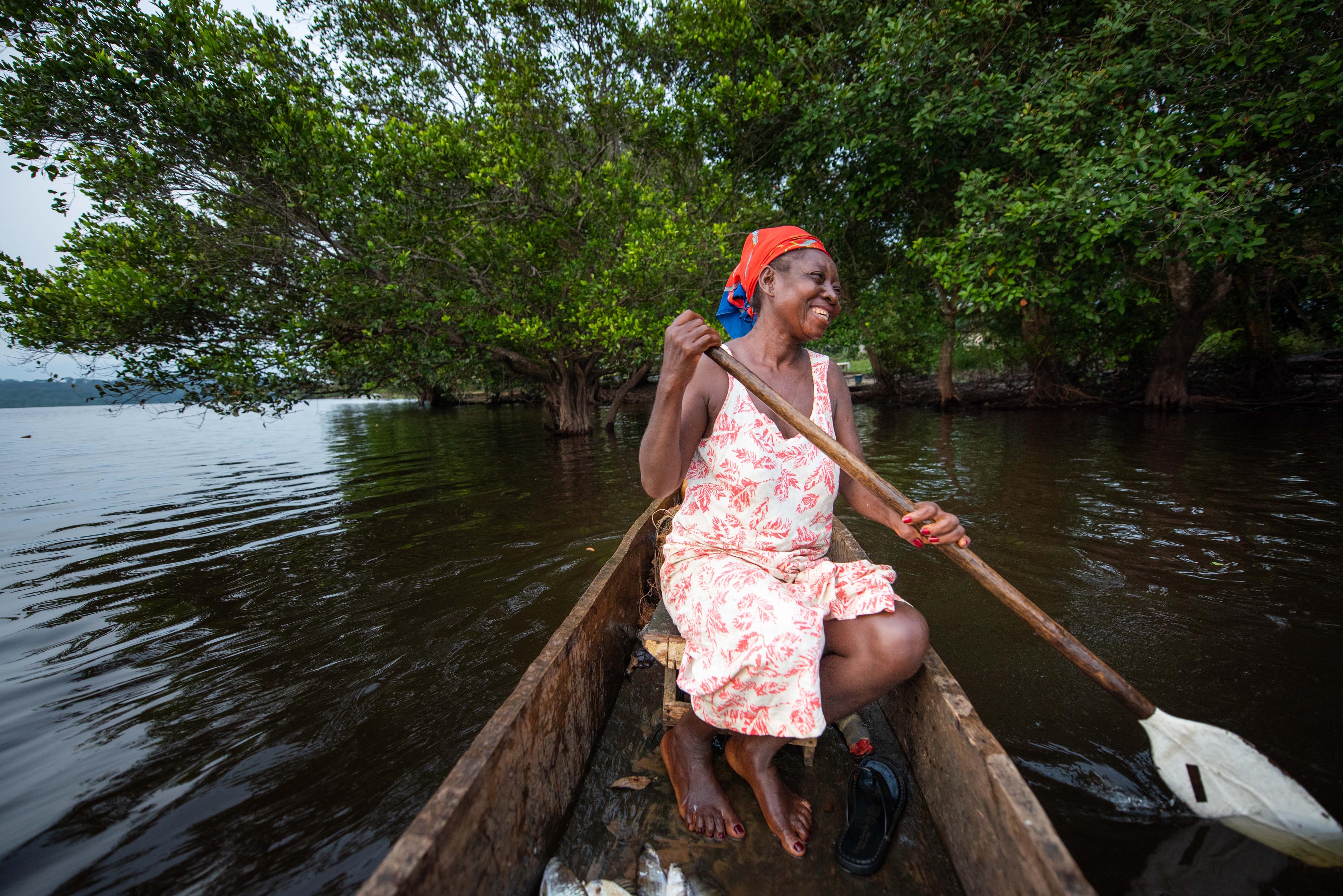 A woman sits in a small wooden boat and paddles.